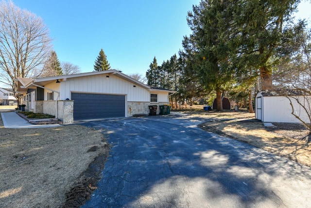 view of property exterior featuring stone siding, aphalt driveway, an attached garage, and a shed