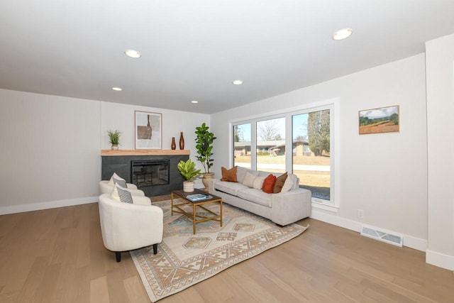 living room featuring a glass covered fireplace, wood finished floors, visible vents, and baseboards