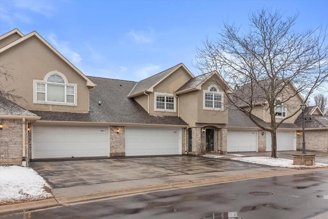 view of front of house with driveway, brick siding, roof with shingles, and stucco siding