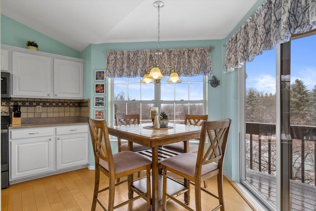 dining area with light wood-type flooring, a notable chandelier, and vaulted ceiling