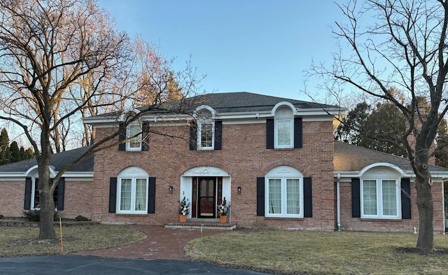 colonial inspired home with roof with shingles, brick siding, and a front lawn