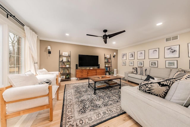 living room featuring baseboards, visible vents, light wood-style flooring, ceiling fan, and crown molding