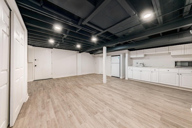 finished basement featuring freestanding refrigerator, baseboards, a sink, and light wood finished floors