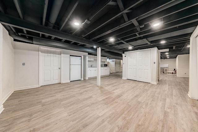 finished below grade area featuring freestanding refrigerator, light wood-style flooring, and baseboards