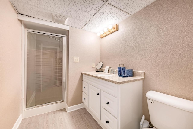 bathroom featuring a paneled ceiling, a textured wall, toilet, a shower stall, and wood finished floors