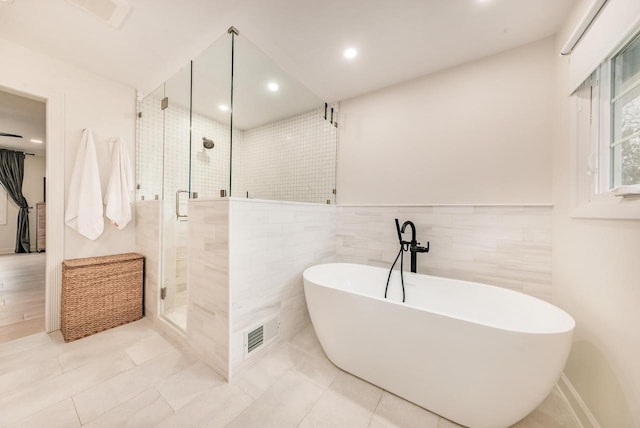 full bath featuring tile walls, recessed lighting, a soaking tub, visible vents, and a stall shower