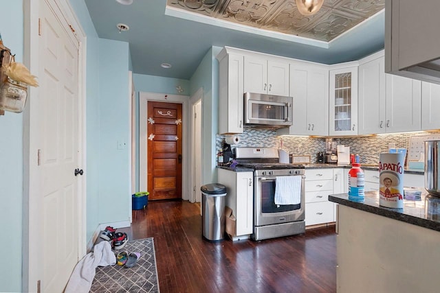 kitchen with an ornate ceiling, dark wood-style floors, decorative backsplash, appliances with stainless steel finishes, and white cabinets