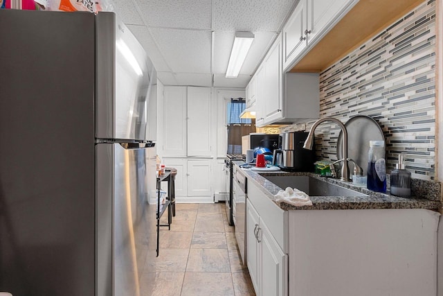 kitchen with decorative backsplash, appliances with stainless steel finishes, a paneled ceiling, white cabinetry, and a sink