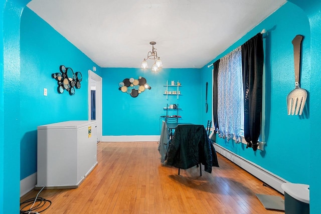 dining space featuring baseboards, a baseboard radiator, hardwood / wood-style flooring, and an inviting chandelier