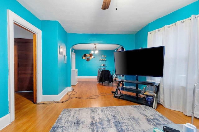 living area with arched walkways, wood finished floors, a ceiling fan, and baseboards