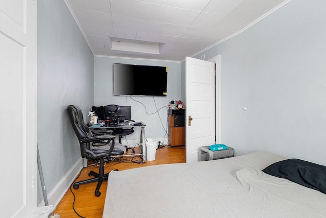 bedroom featuring baseboards, wood finished floors, and crown molding