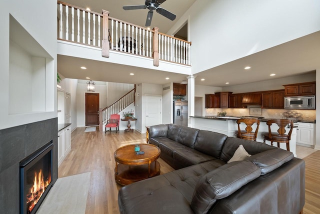 living room featuring light wood-style floors, a fireplace, a towering ceiling, and stairs