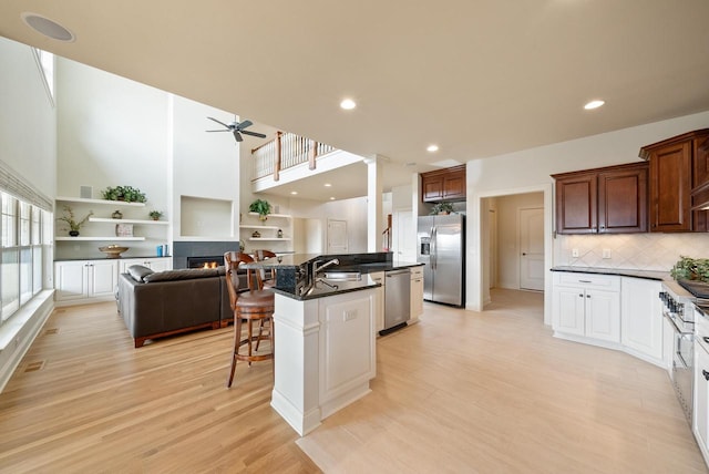 kitchen with a tile fireplace, stainless steel appliances, a sink, light wood finished floors, and a kitchen bar