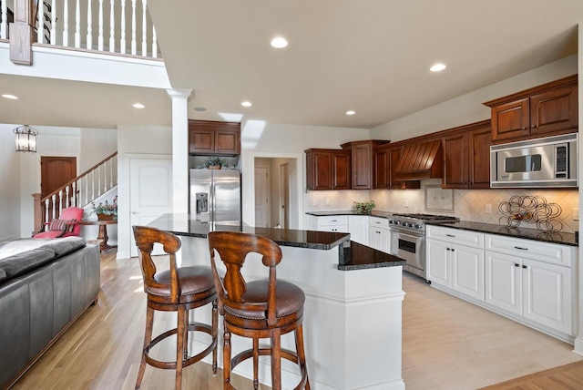 kitchen with a breakfast bar area, custom exhaust hood, decorative backsplash, appliances with stainless steel finishes, and a kitchen island