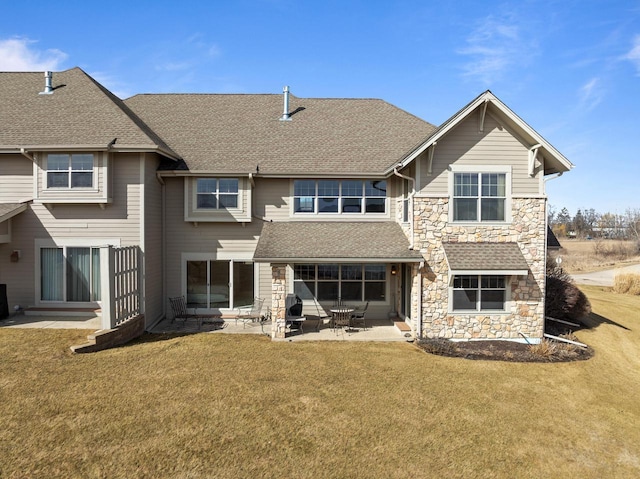 rear view of property with a yard, stone siding, a patio area, and a shingled roof