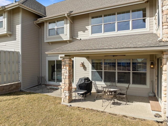 back of property featuring a shingled roof, fence, a lawn, and a patio