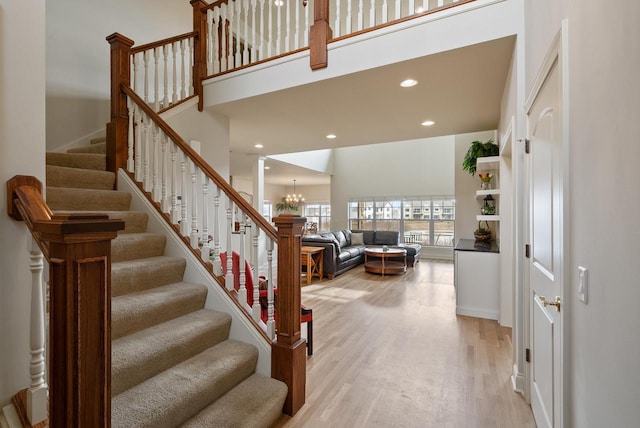 stairway featuring a towering ceiling, a chandelier, wood finished floors, and recessed lighting