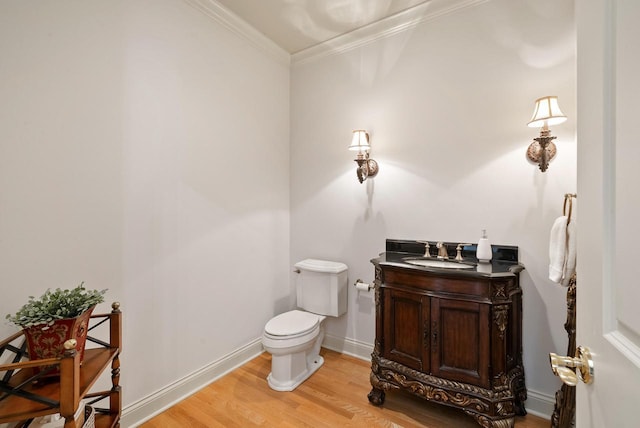 half bath with baseboards, toilet, wood finished floors, crown molding, and vanity