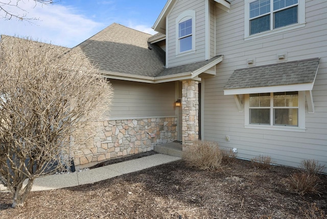 entrance to property with stone siding and a shingled roof