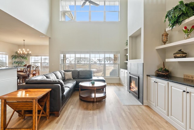 living room featuring ceiling fan with notable chandelier, light wood-type flooring, a fireplace with flush hearth, and a towering ceiling