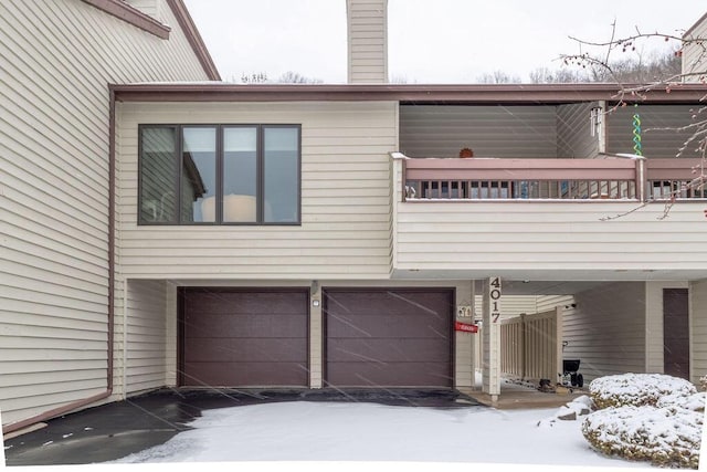 snow covered property featuring a balcony, a garage, and a chimney