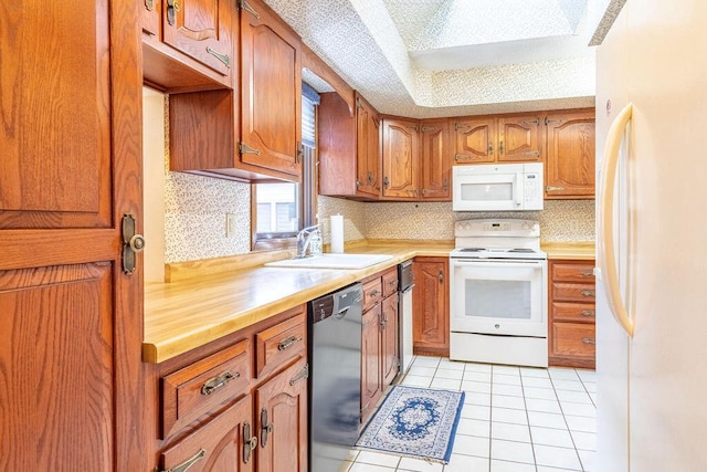 kitchen with brown cabinets, light countertops, light tile patterned flooring, a sink, and white appliances