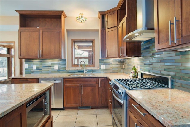 kitchen featuring a wealth of natural light, a sink, appliances with stainless steel finishes, wall chimney exhaust hood, and light stone countertops