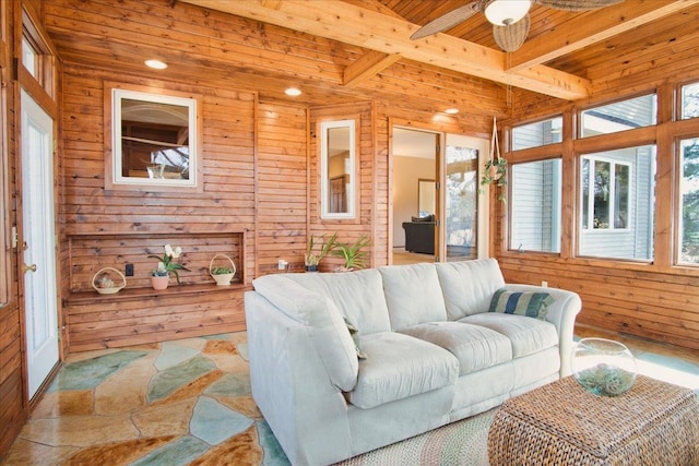 living area featuring wooden walls, beamed ceiling, wooden ceiling, and ceiling fan