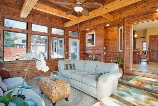 living area with wooden walls, a ceiling fan, tile patterned flooring, wooden ceiling, and beamed ceiling