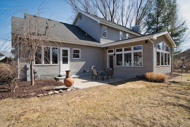 back of house featuring a patio area, a lawn, roof with shingles, and a chimney