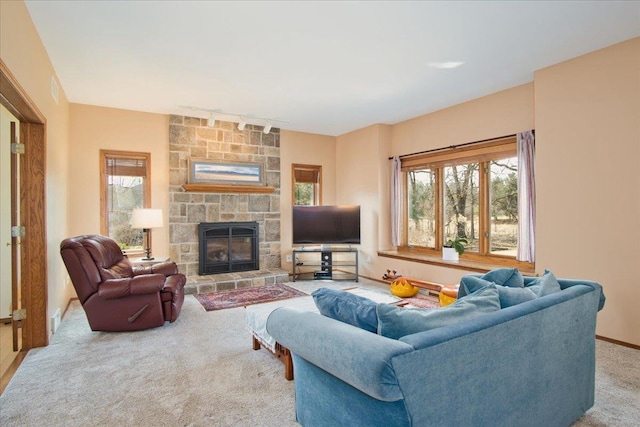 living room with baseboards, carpet flooring, a stone fireplace, and track lighting