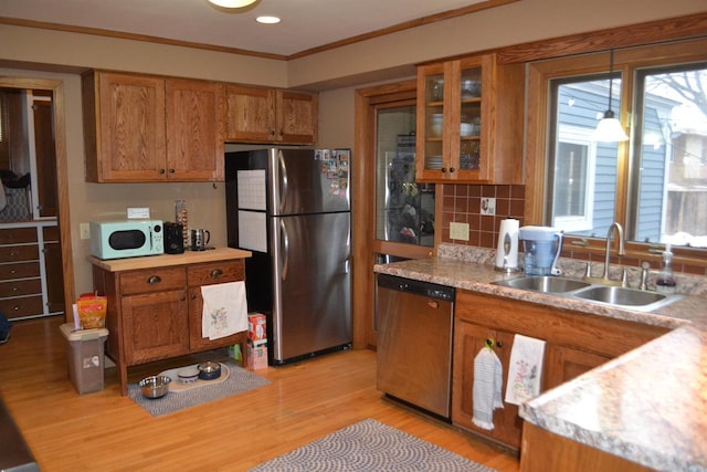 kitchen with light wood finished floors, stainless steel appliances, light countertops, brown cabinetry, and a sink