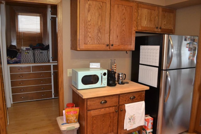 kitchen with white microwave, brown cabinetry, wood finished floors, and freestanding refrigerator