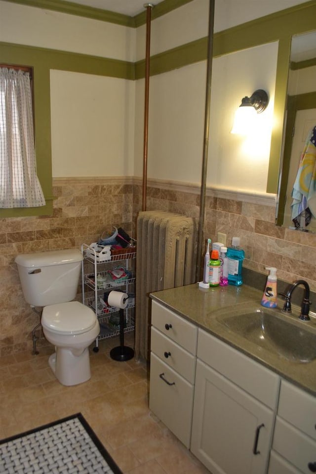 bathroom with toilet, vanity, tile walls, wainscoting, and radiator heating unit