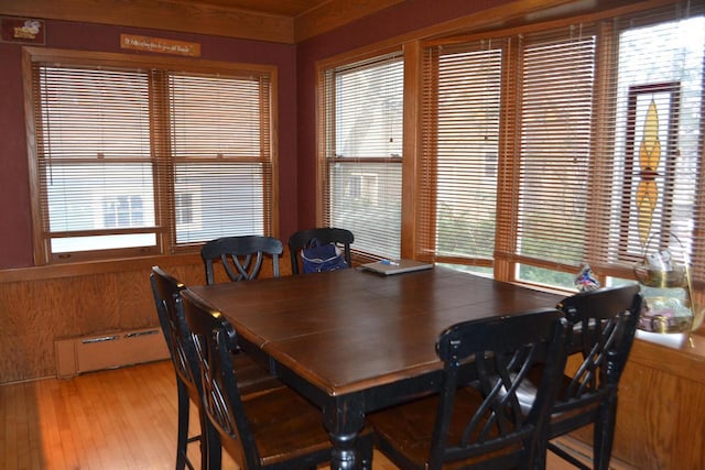 dining space with a healthy amount of sunlight, light wood-style flooring, wooden walls, and a baseboard heating unit