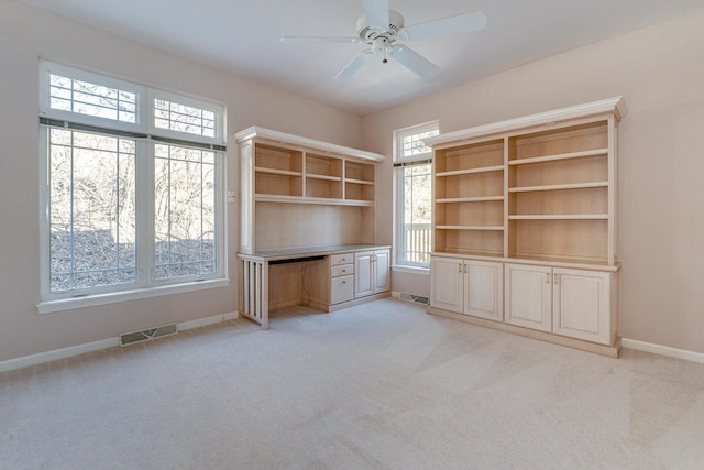 unfurnished office with visible vents, baseboards, ceiling fan, light carpet, and built in desk