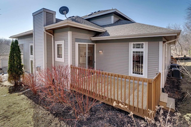 view of front of house with a wooden deck, central AC unit, a chimney, and a shingled roof