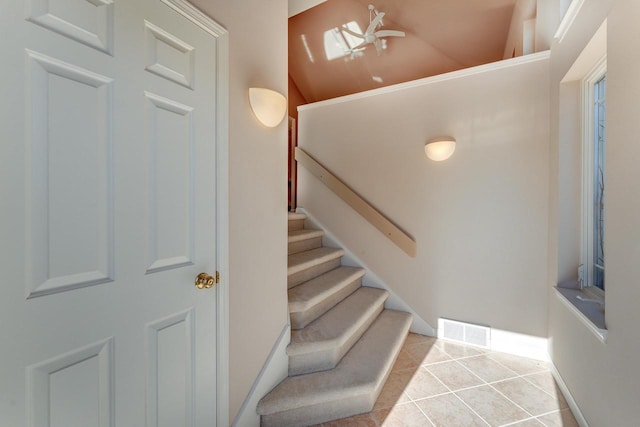 staircase featuring tile patterned floors, baseboards, visible vents, and vaulted ceiling