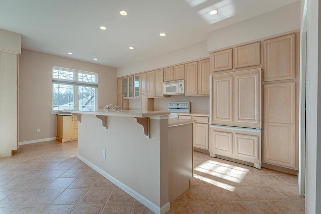 kitchen with white microwave, light brown cabinetry, light countertops, electric stove, and a kitchen bar