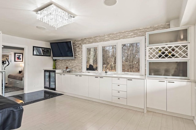 kitchen featuring white cabinets, light wood-style flooring, wine cooler, light countertops, and a sink