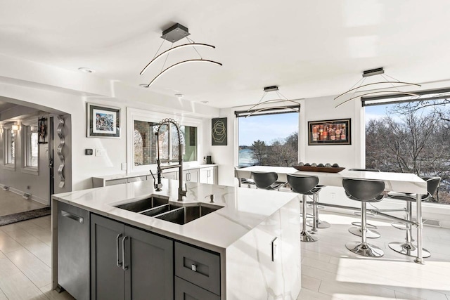 kitchen with arched walkways, dishwasher, light stone countertops, a kitchen island with sink, and a sink