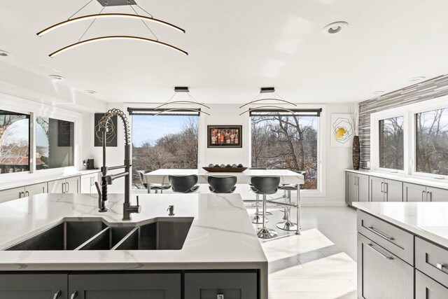 kitchen featuring light stone countertops, plenty of natural light, a sink, and gray cabinetry