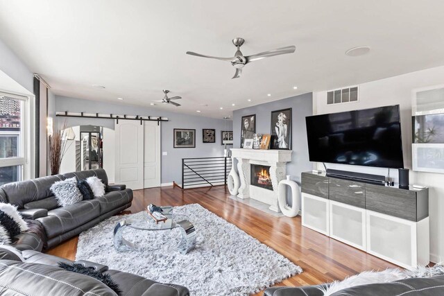 living area with a barn door, visible vents, a ceiling fan, a fireplace with flush hearth, and wood finished floors