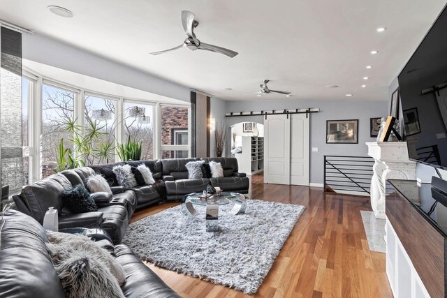 living area featuring ceiling fan, a barn door, arched walkways, and wood finished floors