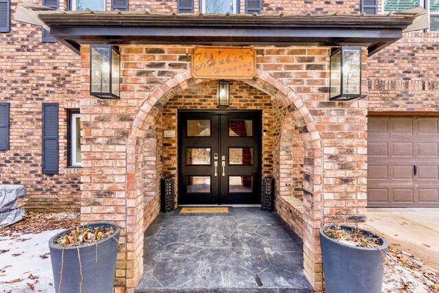 entrance to property featuring a garage, french doors, and brick siding