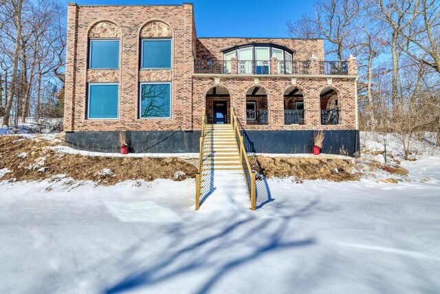 view of front of home with brick siding, stairway, and a balcony