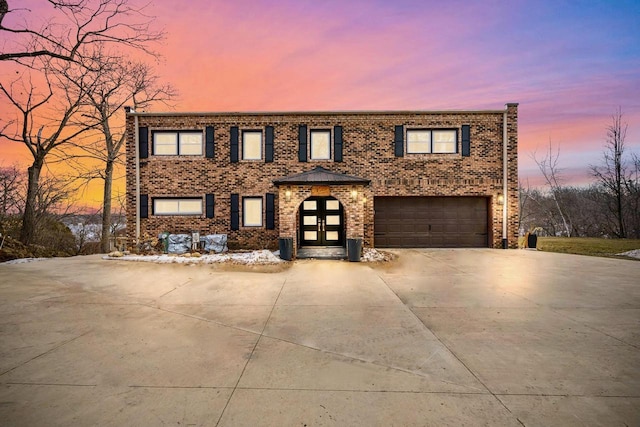 view of front of house with driveway, brick siding, an attached garage, and french doors