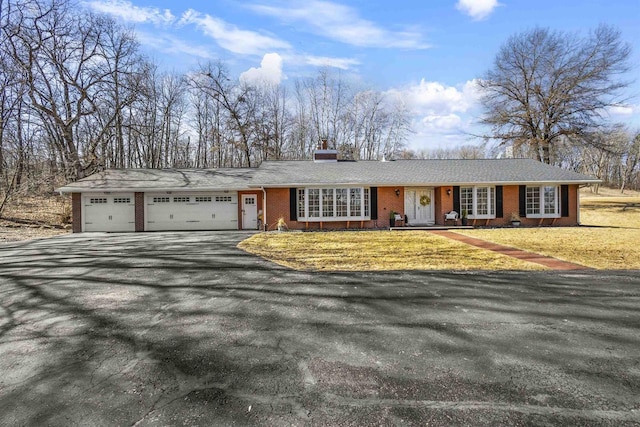 ranch-style house with brick siding, a front lawn, aphalt driveway, a chimney, and a garage