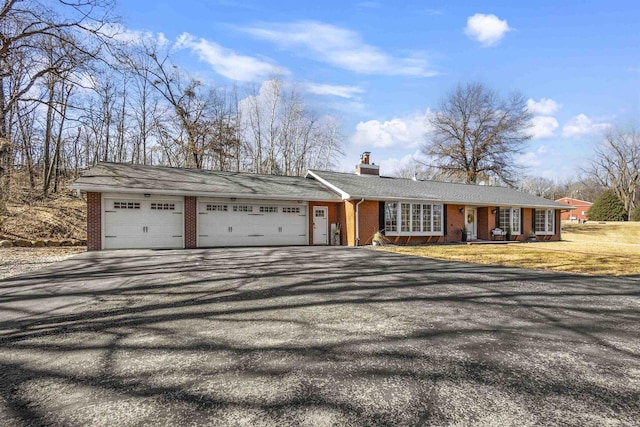 ranch-style house with brick siding, a front yard, a chimney, a garage, and driveway