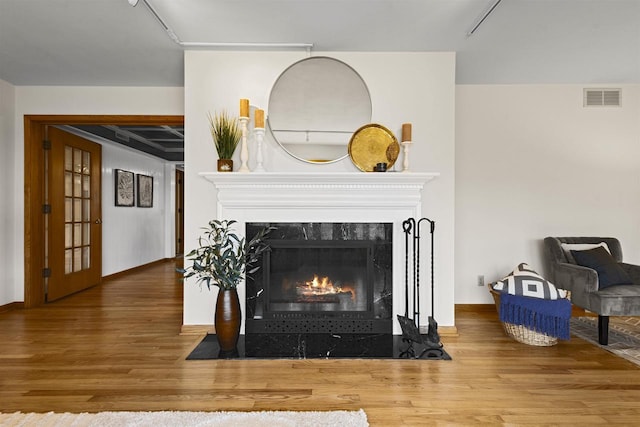 room details featuring a high end fireplace, visible vents, baseboards, and wood finished floors